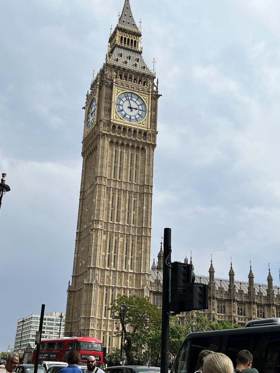 Big Ben against a cloudy sky, with people and a red bus in the foreground.
