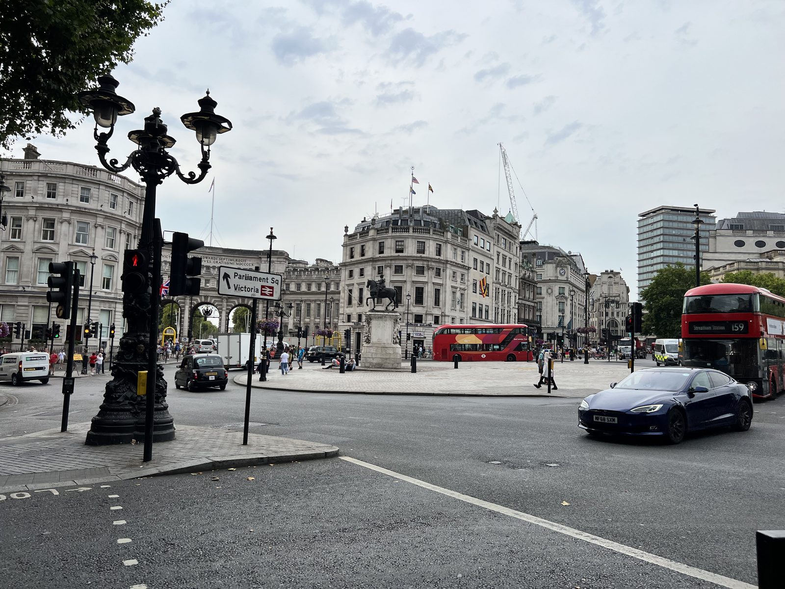 Street view with red double-decker buses, cars, and pedestrians, historical buildings behind.